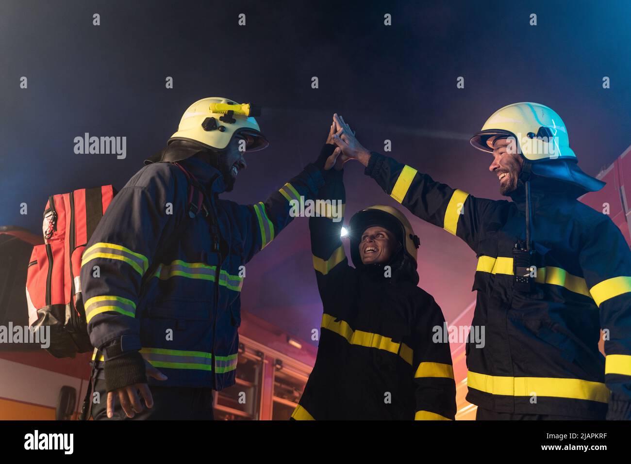 I vigili del fuoco felici uomini e donne dopo l'azione riuscita con camion del fuoco in background alla notte Foto Stock