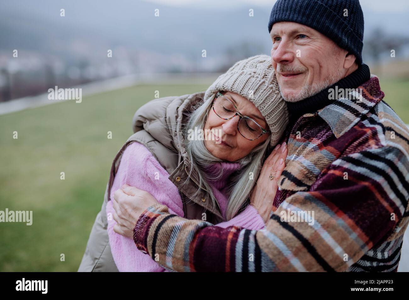 Uomo anziano abbracciando e consolando la sua moglie sconvolta all'aperto in giardino in inverno. Foto Stock