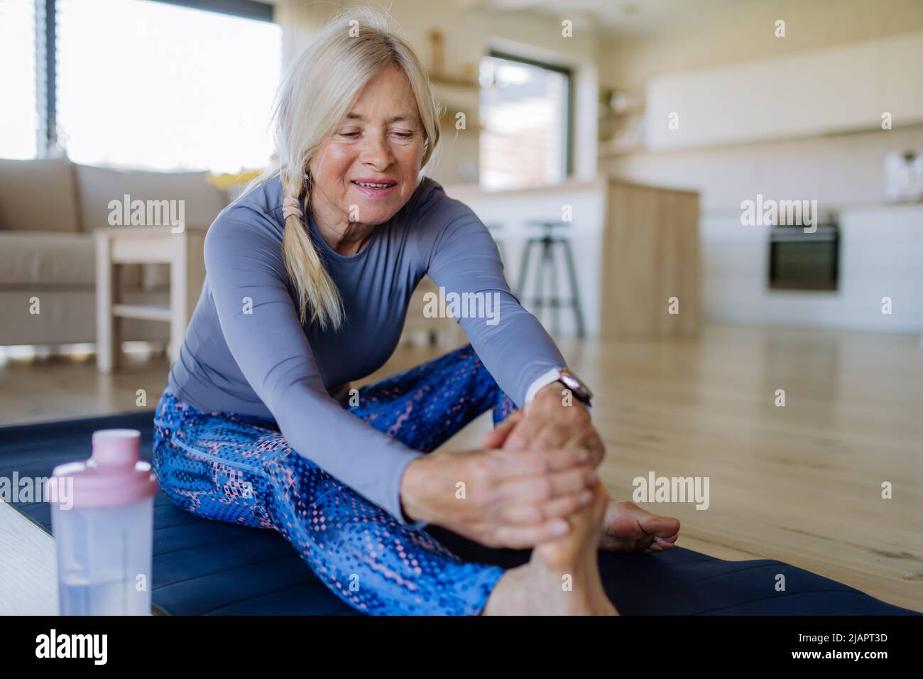 Misura la donna anziana facendo esercizio stretching a casa, concetto di stile di vita attivo. Foto Stock
