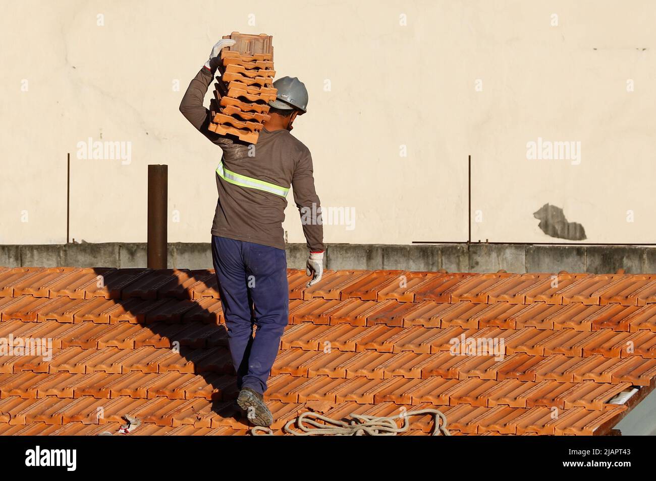 Uomo lavoro sul montaggio della copertura. Costruzione del tetto. Riparazione del tetto in muratura. Casa in costruzione. Il Workman rinnova il tetto impermeabilizzante dell'edificio. Foto Stock