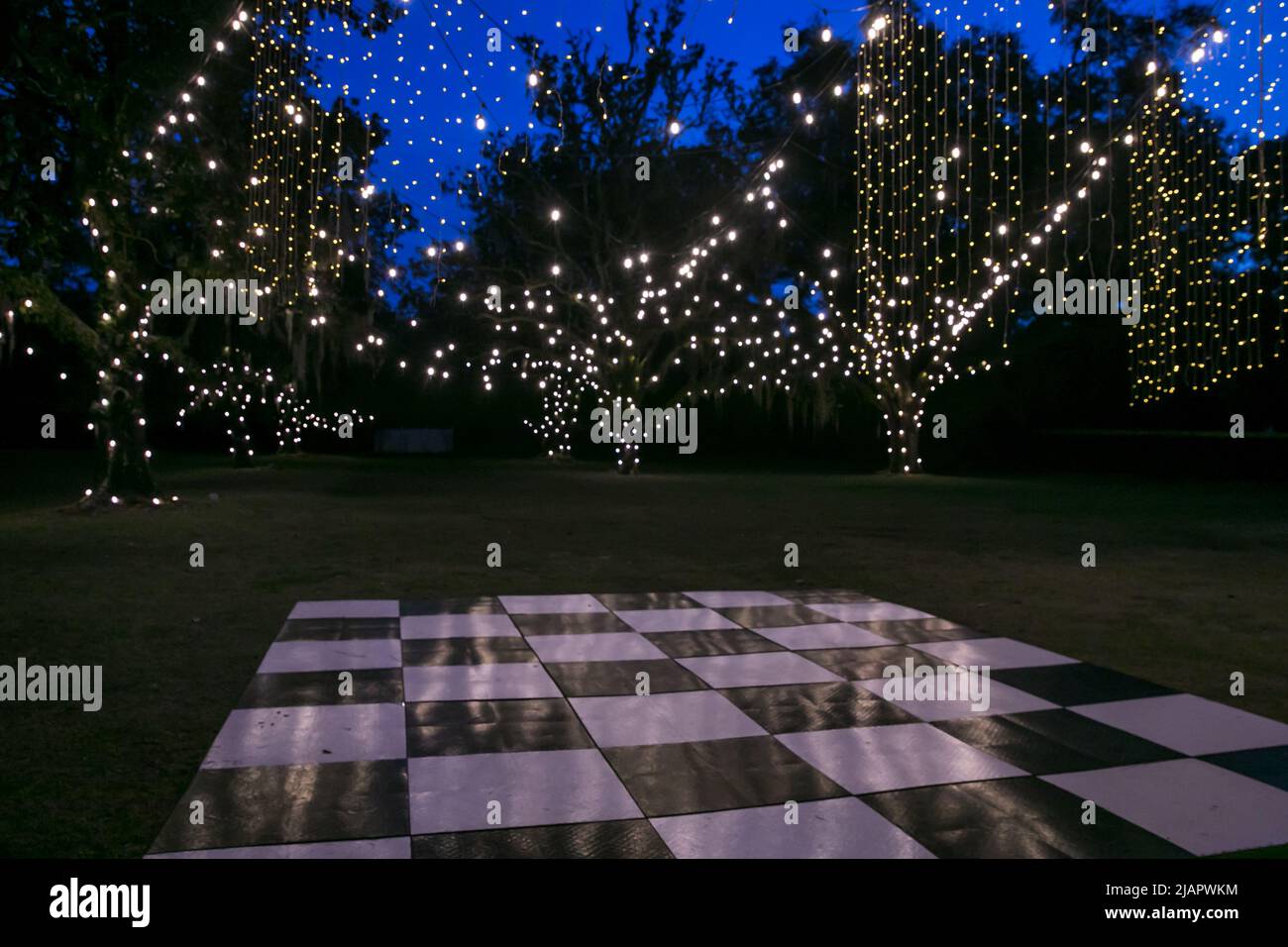 Grande pista da ballo esterna a scacchiera per una festa, un matrimonio, un evento o un ricevimento di notte con luci scintillanti a corda Foto Stock