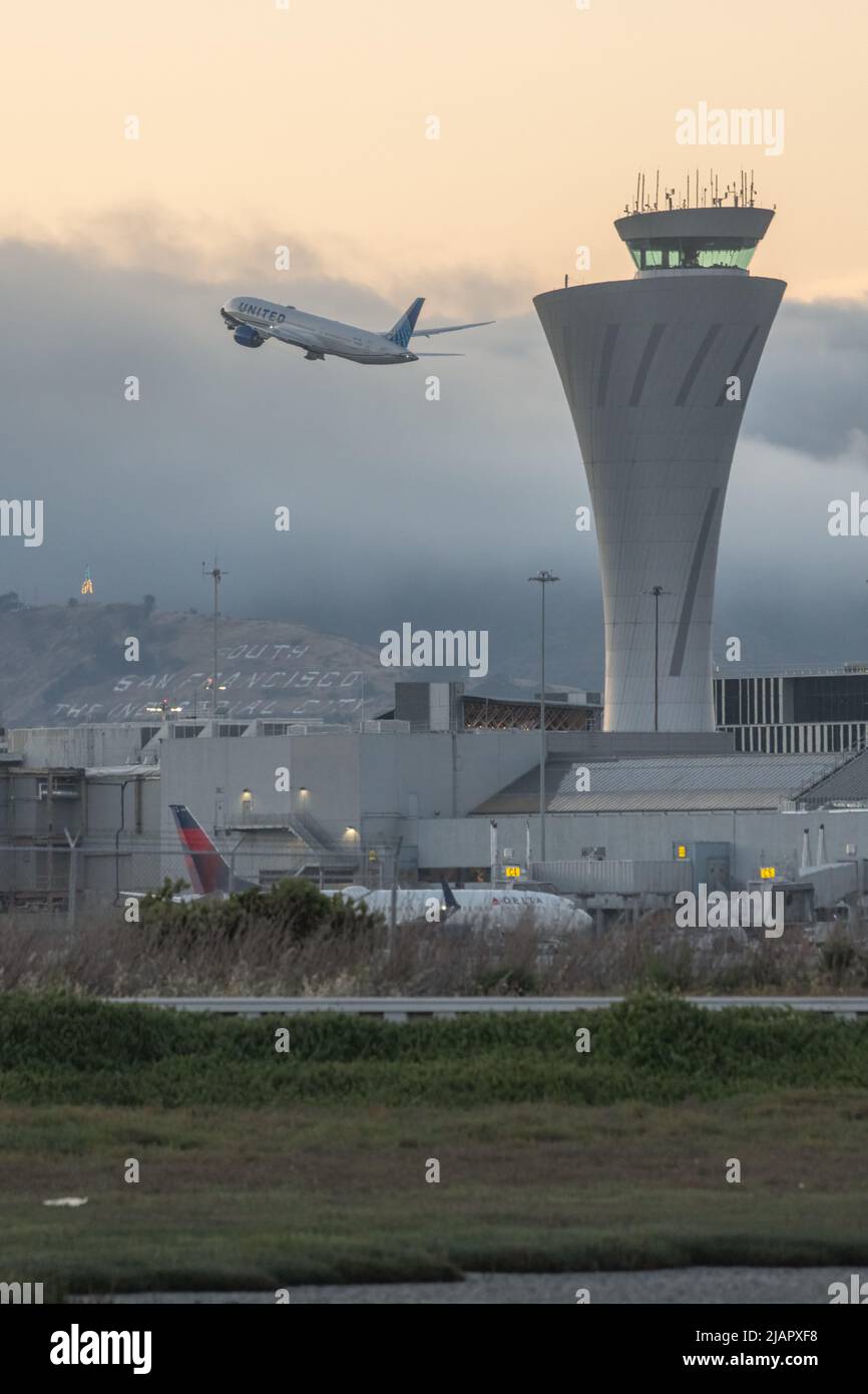 La torre di controllo del traffico dell'aeroporto internazionale di San Francisco (SFO) nell'area della Baia della California con un aereo che decollo in background Foto Stock