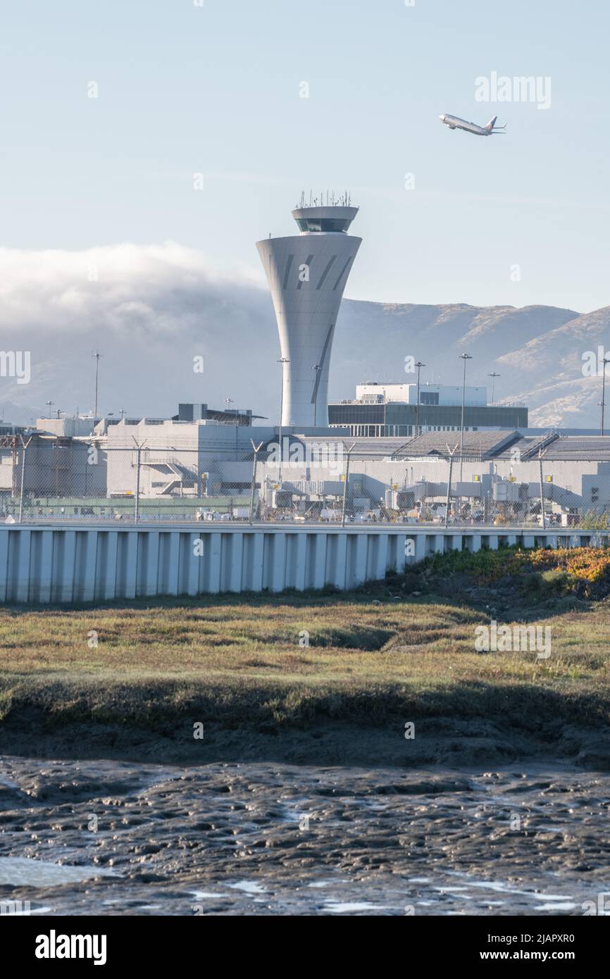 La torre di controllo del traffico dell'aeroporto internazionale di San Francisco (SFO) nell'area della Baia della California con un aereo che decollo in background. Foto Stock