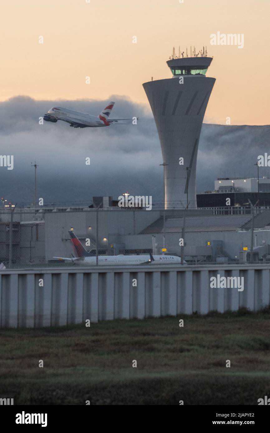 La torre di controllo del traffico dell'aeroporto internazionale di San Francisco (SFO) nell'area della Baia della California con un aereo che decollo in background. Foto Stock