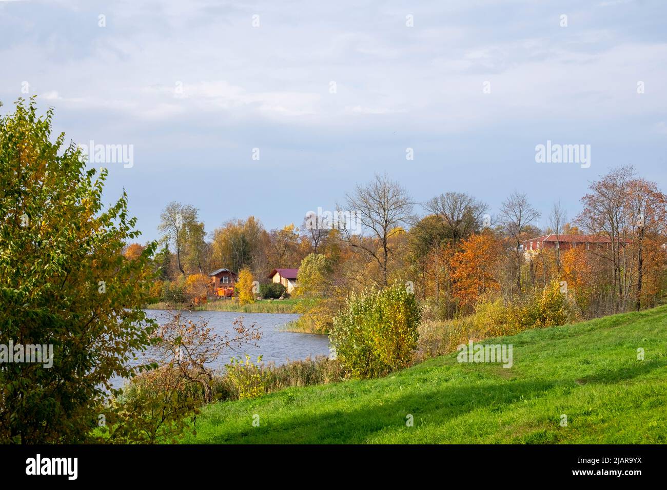 Bella vista sulla natura con un lago e edifici residenziali in campagna con una giornata di sole. Autunno d'oro, bellezza nella natura. Messa a fuoco selettiva. Foto Stock