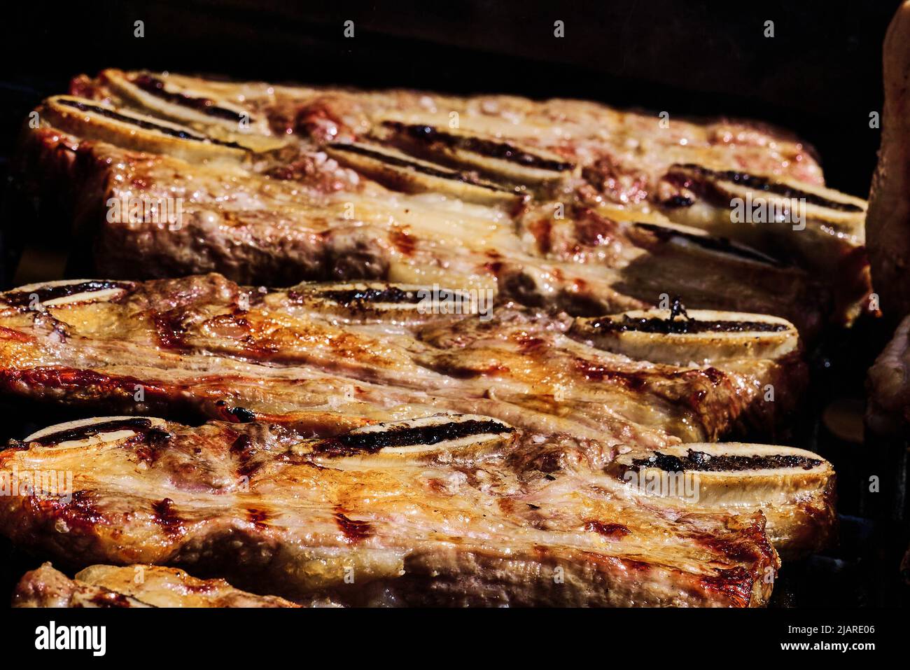 succosa costolette di manzo e costolette di maiale che vengono fatte lentamente sulla griglia sul fuoco ad un barbecue a gas Foto Stock