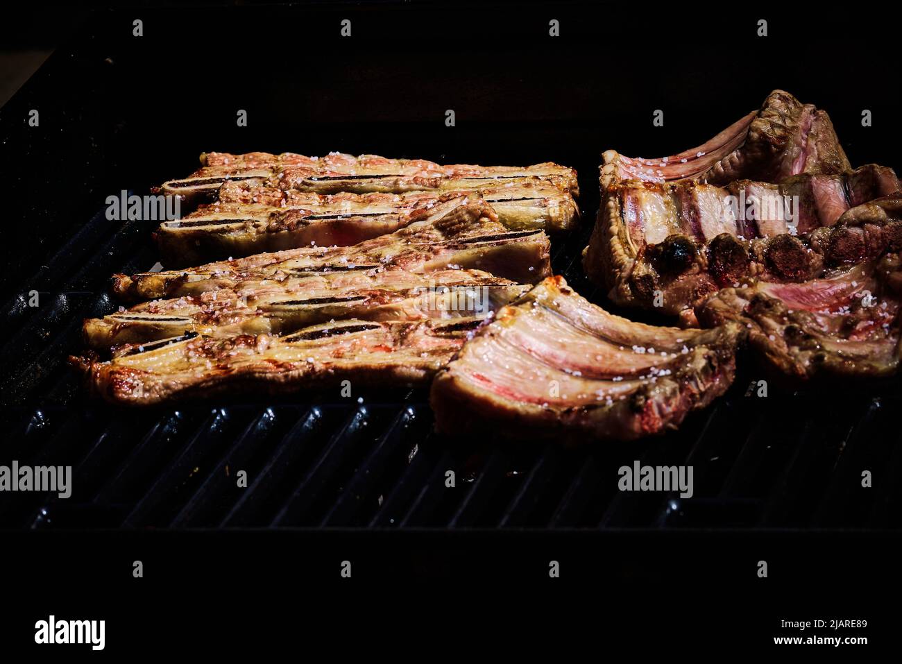 succosa costolette di manzo e costolette di maiale che vengono fatte lentamente sulla griglia sul fuoco ad un barbecue a gas Foto Stock