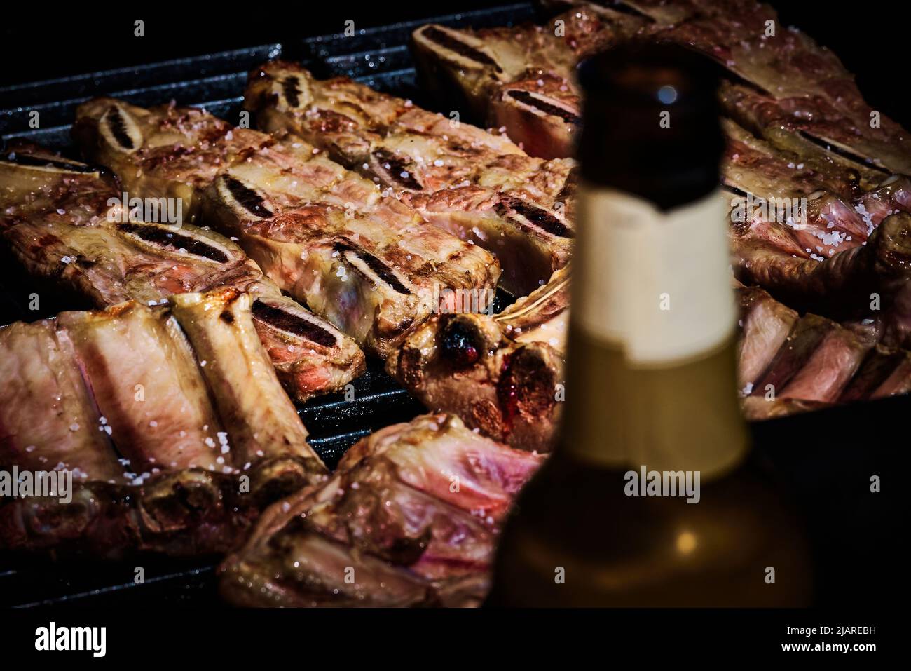 succosa costolette di manzo e costolette di maiale che vengono fatte lentamente sulla griglia sul fuoco ad un barbecue a gas Foto Stock