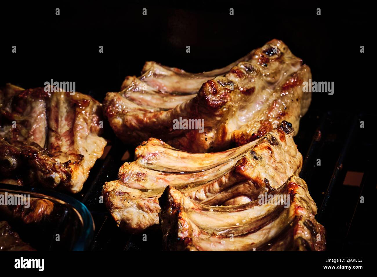 succosa costolette di manzo e costolette di maiale che vengono fatte lentamente sulla griglia sul fuoco ad un barbecue a gas Foto Stock