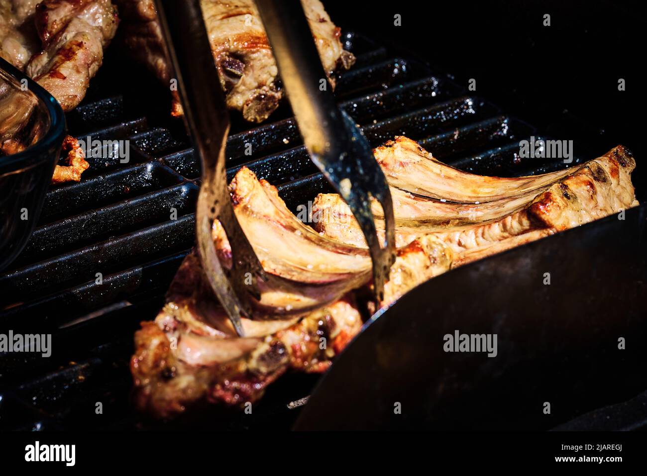 succosa costolette di manzo e costolette di maiale che vengono fatte lentamente sulla griglia sul fuoco ad un barbecue a gas Foto Stock