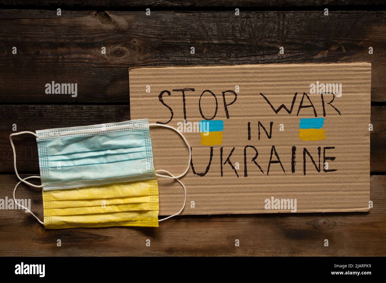 Maschere mediche, giallo e blu, come la bandiera dell'Ucraina, giacciono su un tavolo di legno e un segno con il testo fermare la guerra in Ucraina. Bandiera dello Stato di Ukrain Foto Stock