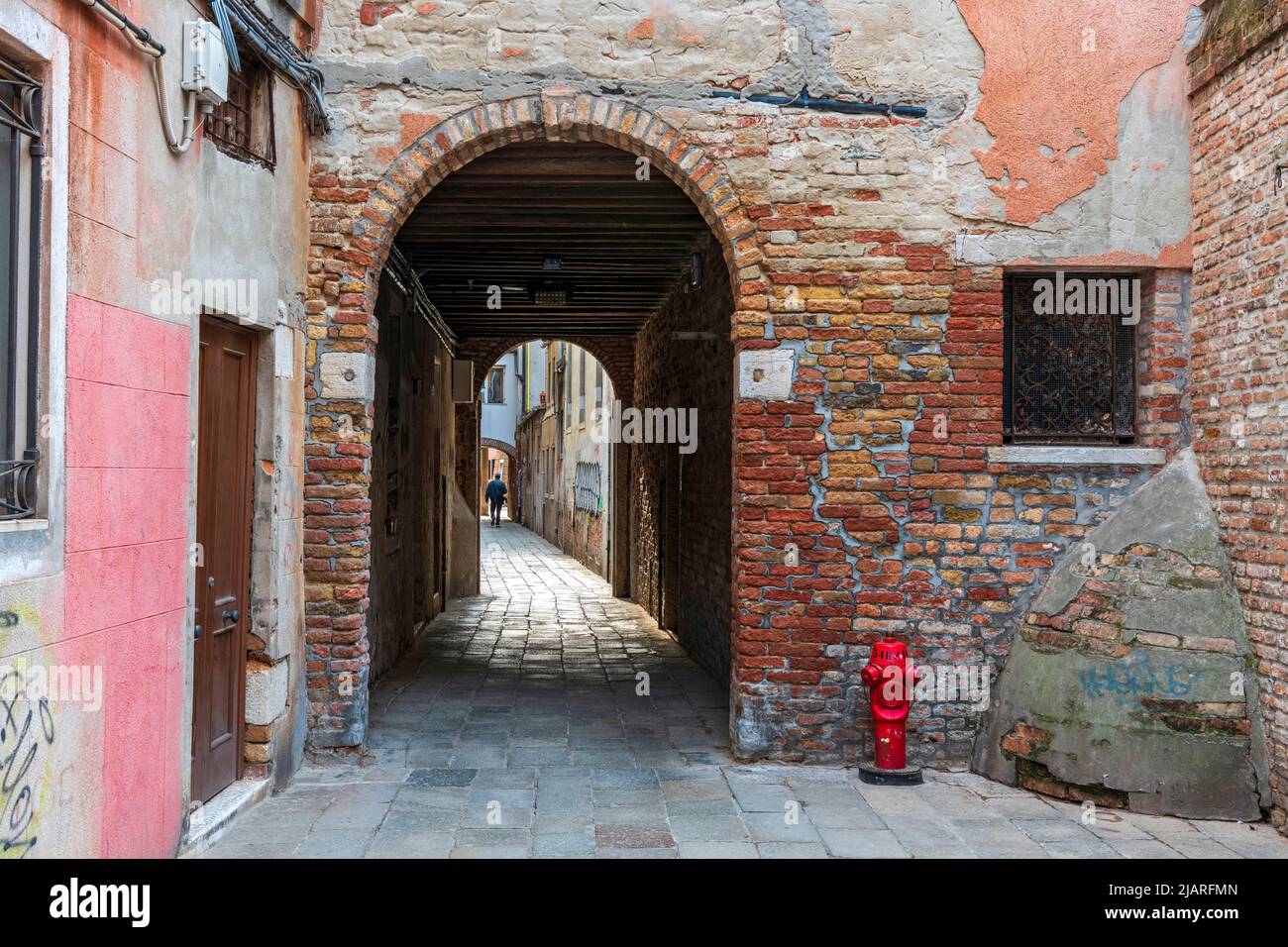 Passaggio sotto due archi, un idrante di fuoco rosso brillante e una parete d'angolo posteriore, retroilluminata dal sole del tardo pomeriggio Foto Stock