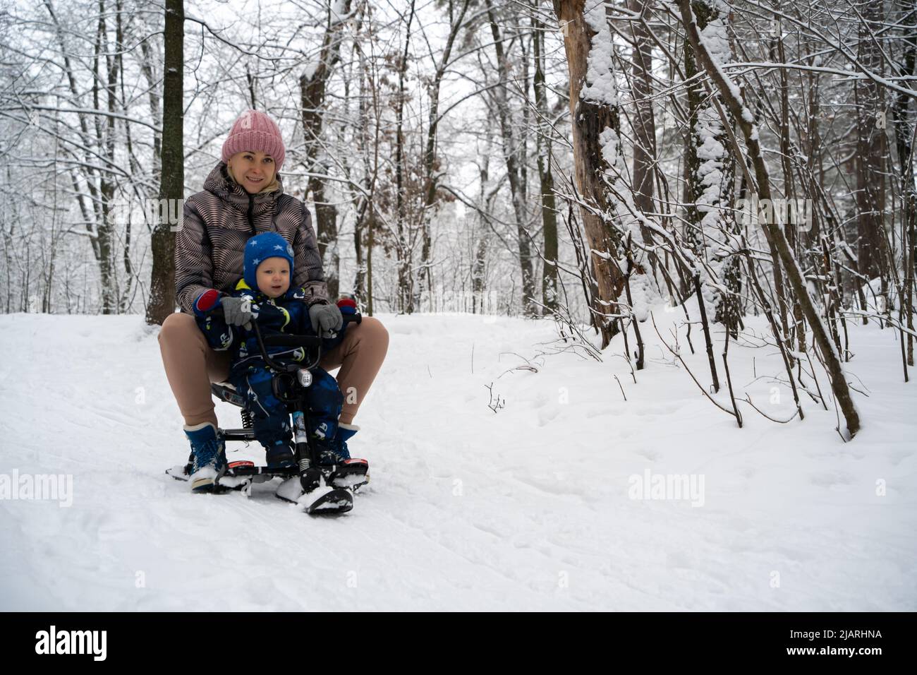 Madre con un bambino su una slitta. Una giovane donna con il suo figlio scivola giù per la collina in una slitta. Famiglia vacanza invernale. Foto Stock