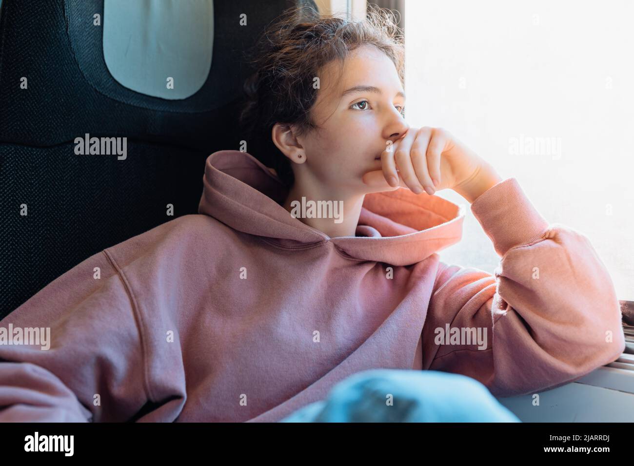 l'adolescente solitario si siede in treno vicino alla finestra, riposando la testa a portata di mano, guarda fuori la finestra, piegando le ginocchia. Lunga corsa in treno, gambe gonfie, viaggio europeo Foto Stock