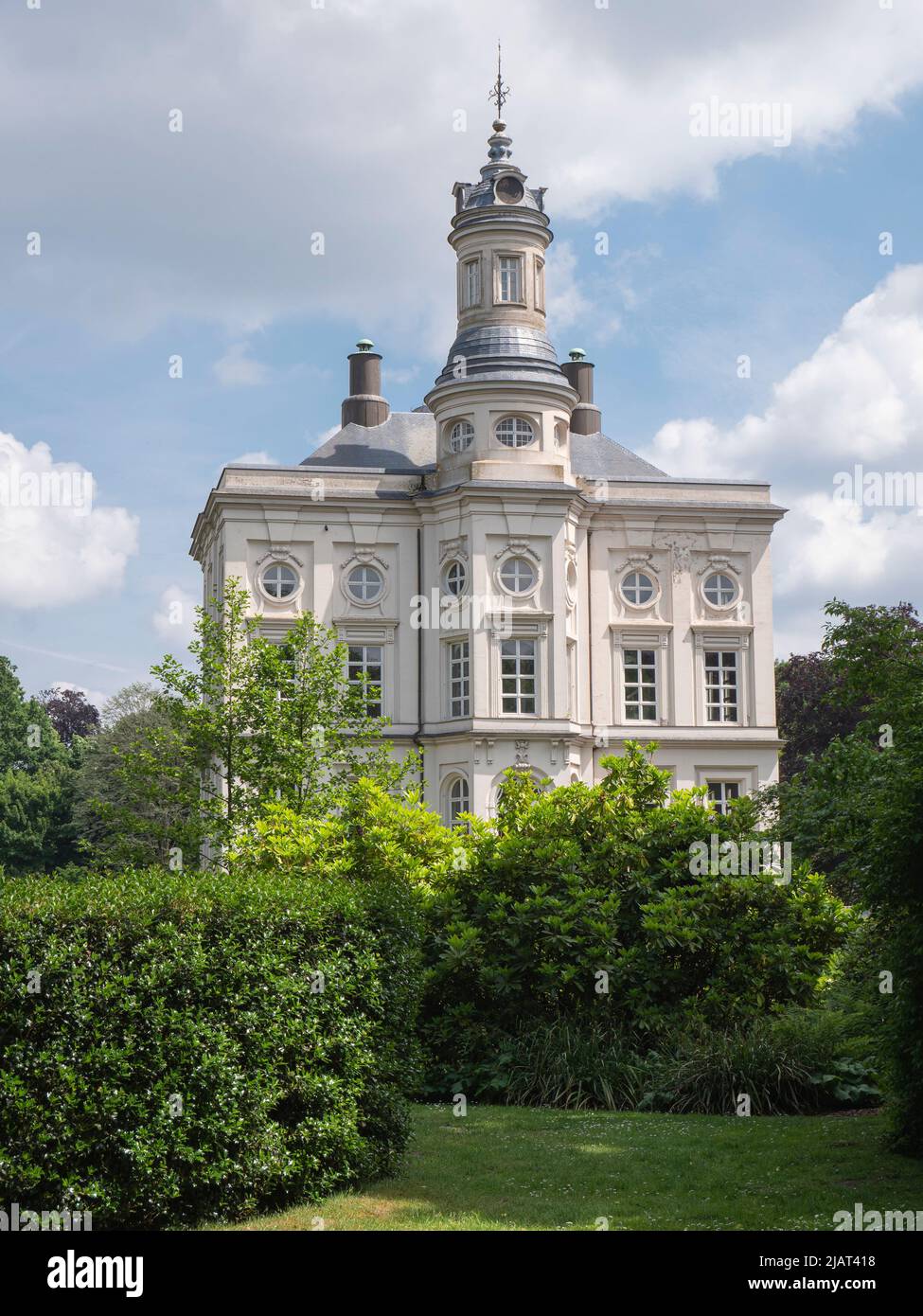 Beveren, Belgio, 22 maggio 2022, castello Hof Ter Saksen, con cielo blu e un campo di nuvole e in primo piano il giardino con piante alte Foto Stock