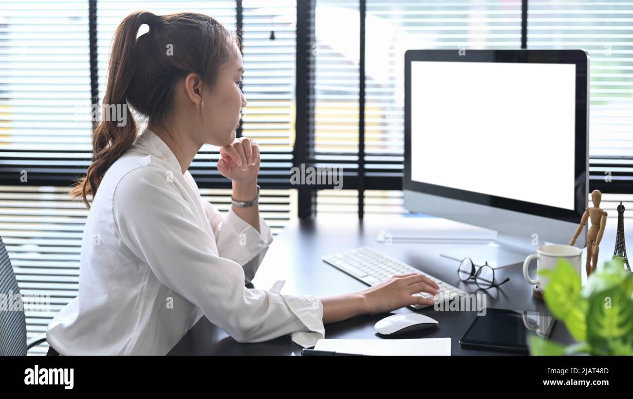 Vista laterale pensieroso manager femminile guardando lo schermo del computer, lavorando in un ambiente di lavoro moderno Foto Stock