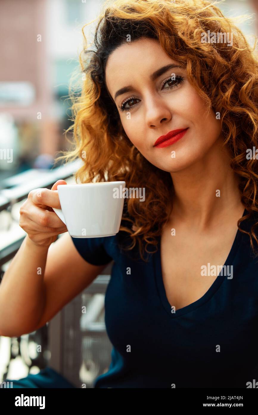 Giovane donna marocchina, con capelli marroni ricci, seduto in un bar all'aperto a Mainz, bere caffè Foto Stock