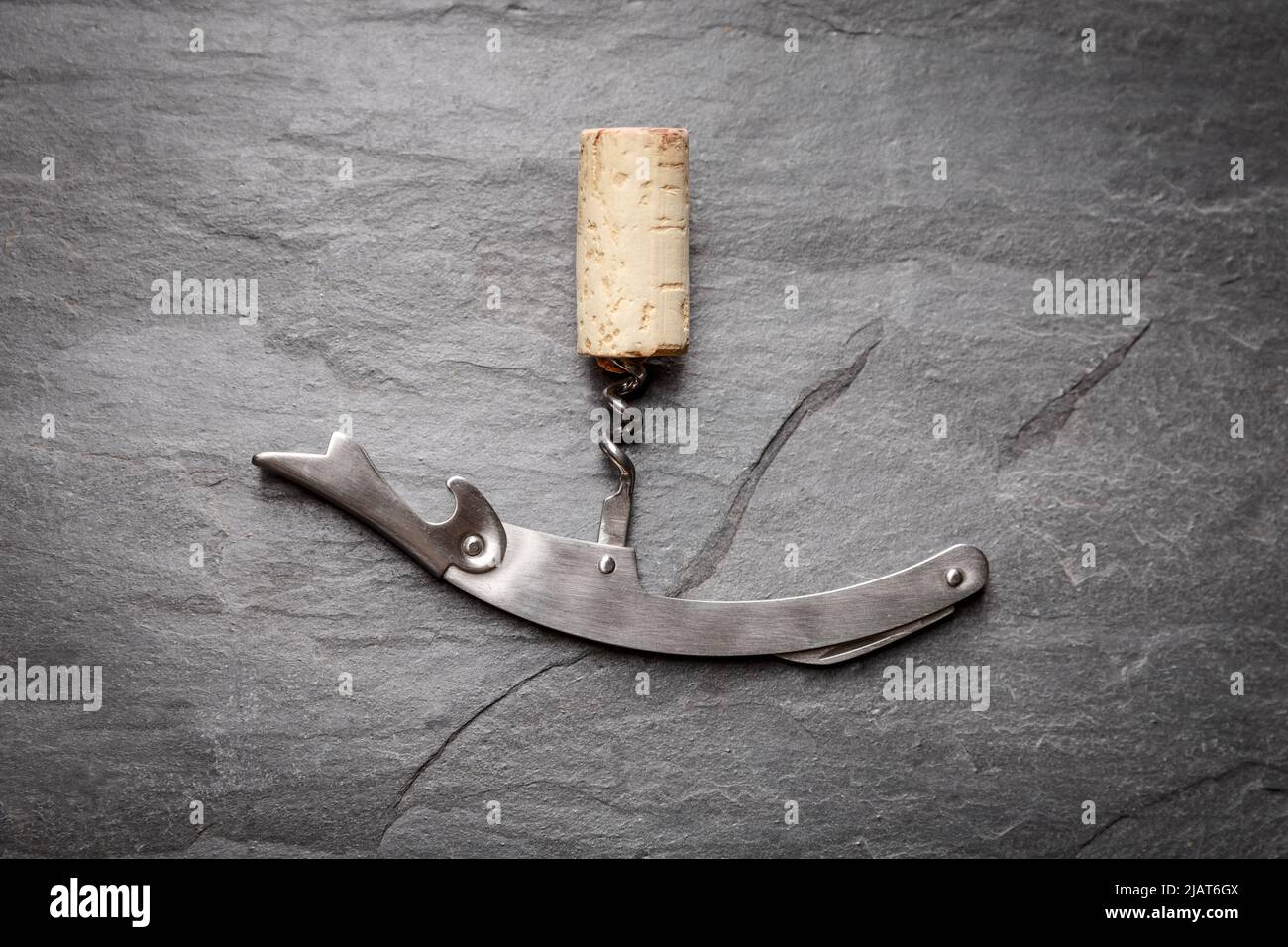 Cavatappi di vino inossidabile con sughero su fondo di ardesia rocciosa nera. Concetto di cultura della vite Foto Stock