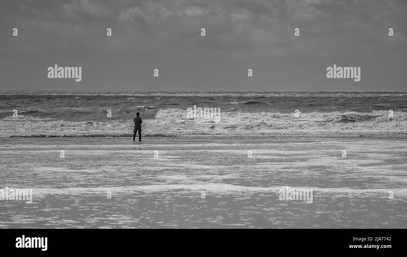 Un pescatore solista, di fronte all'oceano, in una giornata tempestosa. Foto Stock