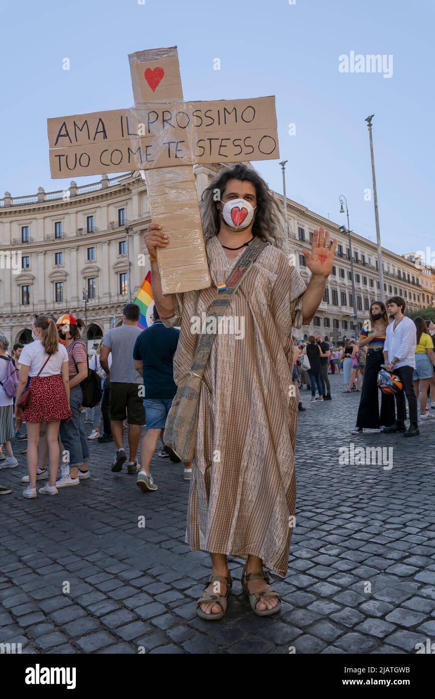 Il giovane vestito come Gesù, con una maschera protettiva con un cuore, tiene una croce di cartone: Amate il vostro prossimo come voi stessi. Gay Pride, Roma, Italia Foto Stock