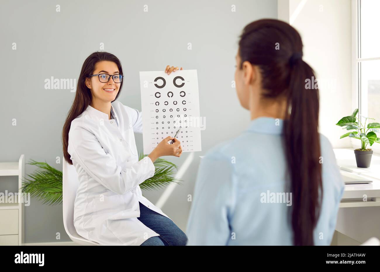 Oftalmologo con l'aiuto di una scheda di test oculare sulla quale mostra lettere controlla la vista della paziente femminile. Foto Stock