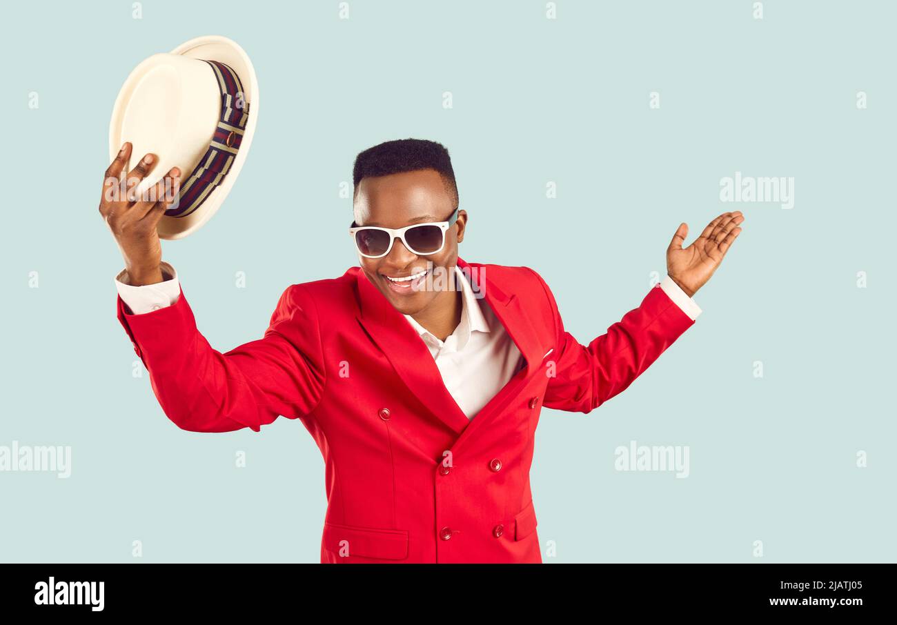 L'uomo africano in abito funky rosso toglie il suo cappello, sorride, fa un arco e vi accoglie a festa Foto Stock