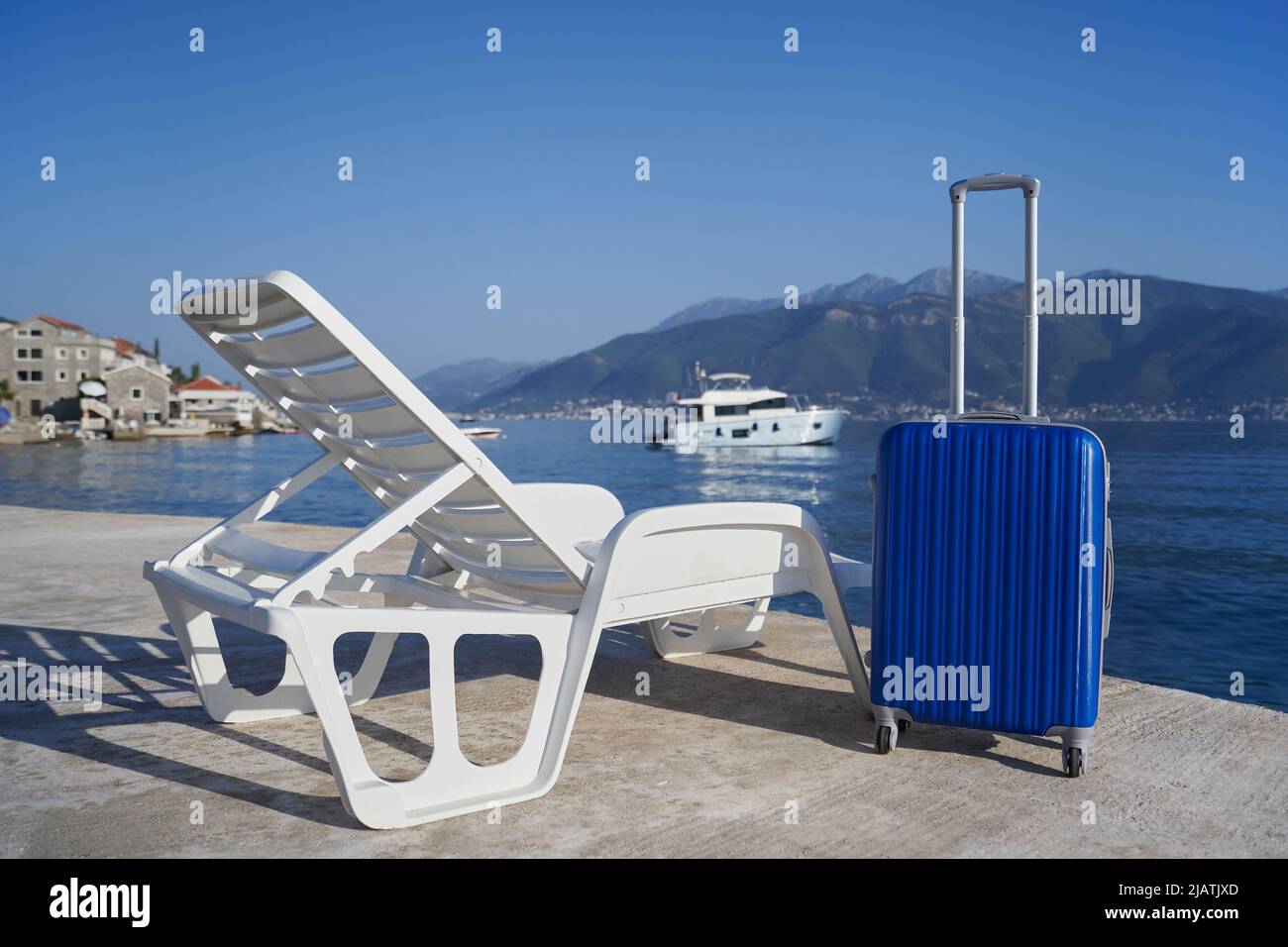 Valigia blu accanto a una sedia da spiaggia contro mare e montagne, concetto di viaggio Foto Stock
