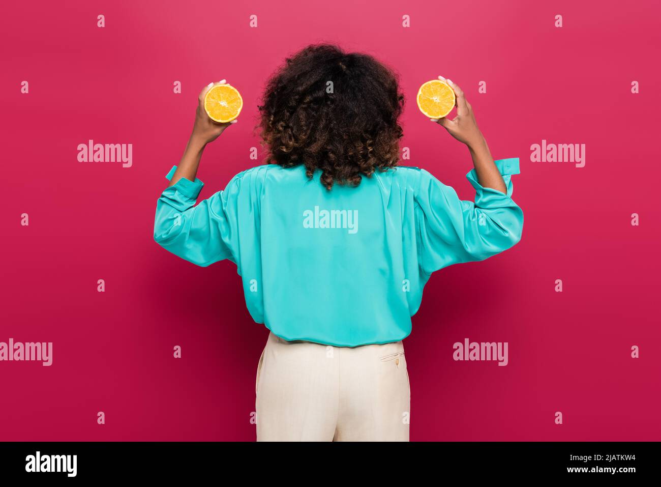 vista posteriore della donna afroamericana in blusa blu che tiene metà arancione isolato su rosa Foto Stock