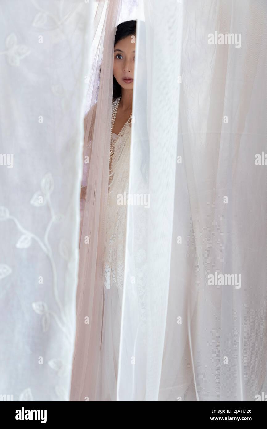 Una bella donna asiatica che indossa un abito in pizzo bianco e posa tra tessuto velato scorrevole Foto Stock