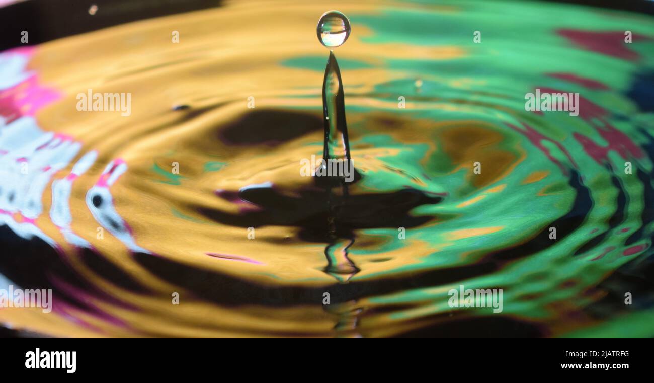 Un primo piano di un tuffo da una goccia d'acqua con sfondo colorato Foto Stock