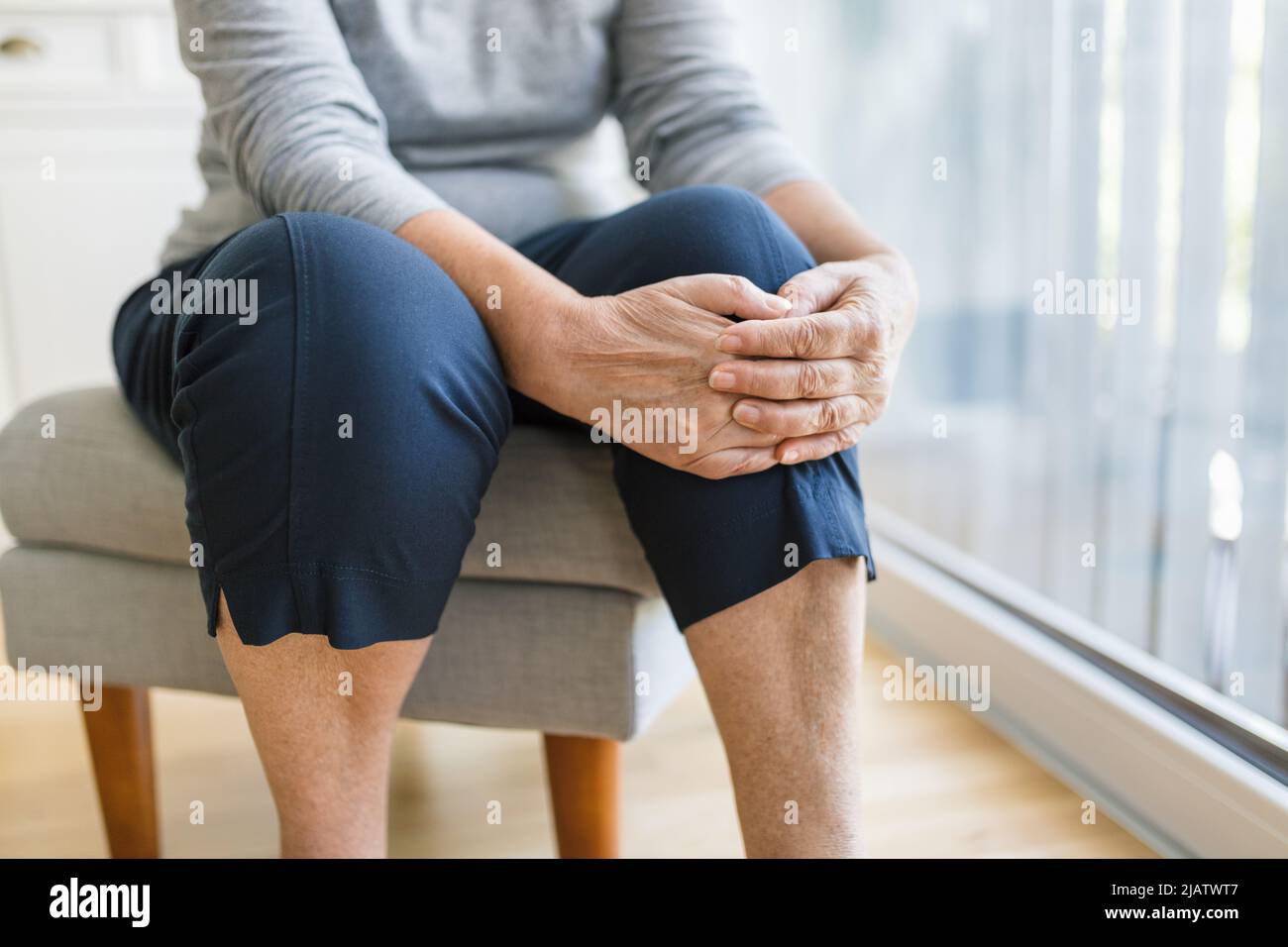 Donna anziana a casa che tiene il suo ginocchio doloroso Foto Stock