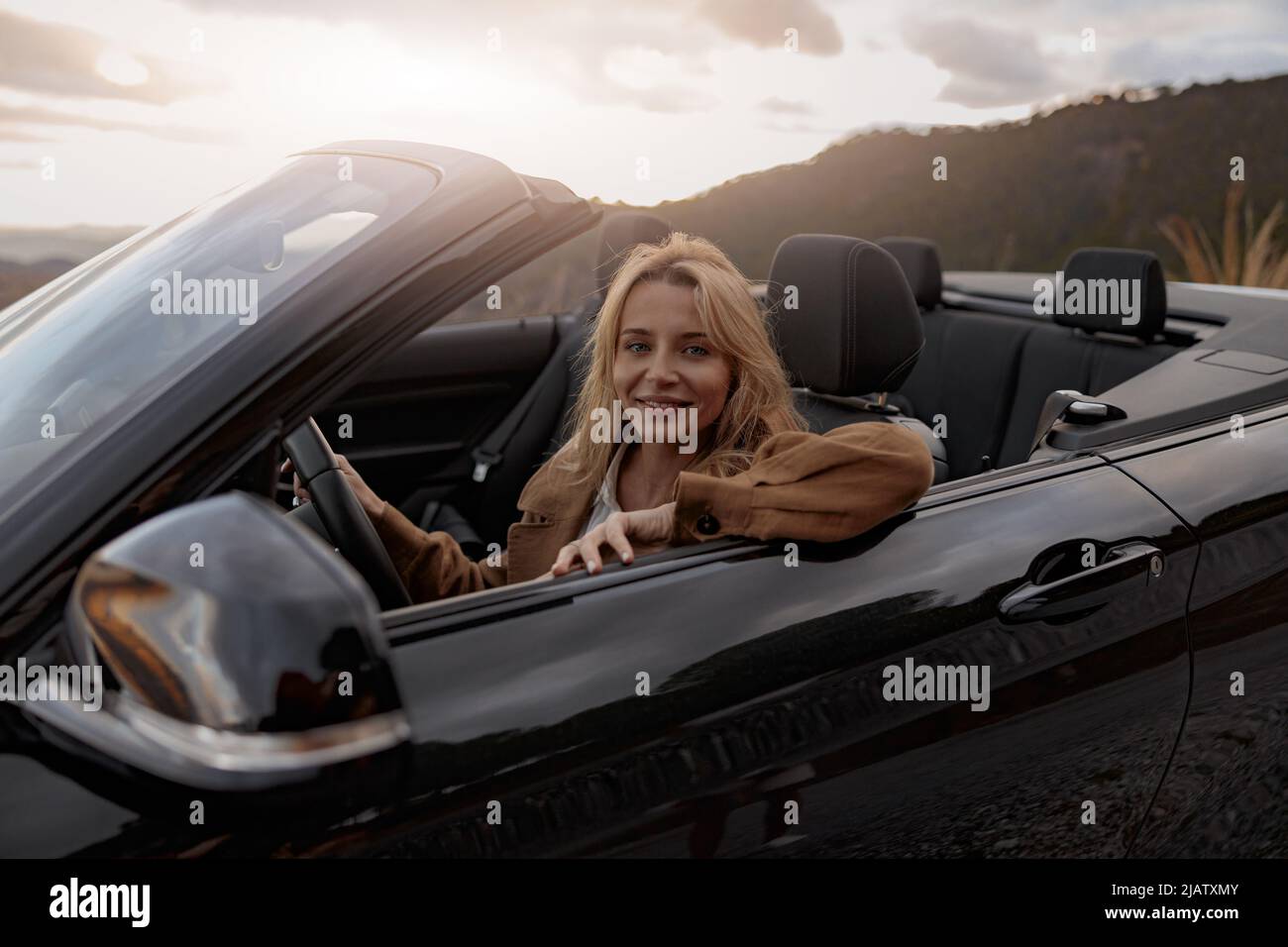 Primo piano di gioiosa giovane bella donna bionda sorridente a macchina fotografica seduta in un'auto convertibile Foto Stock