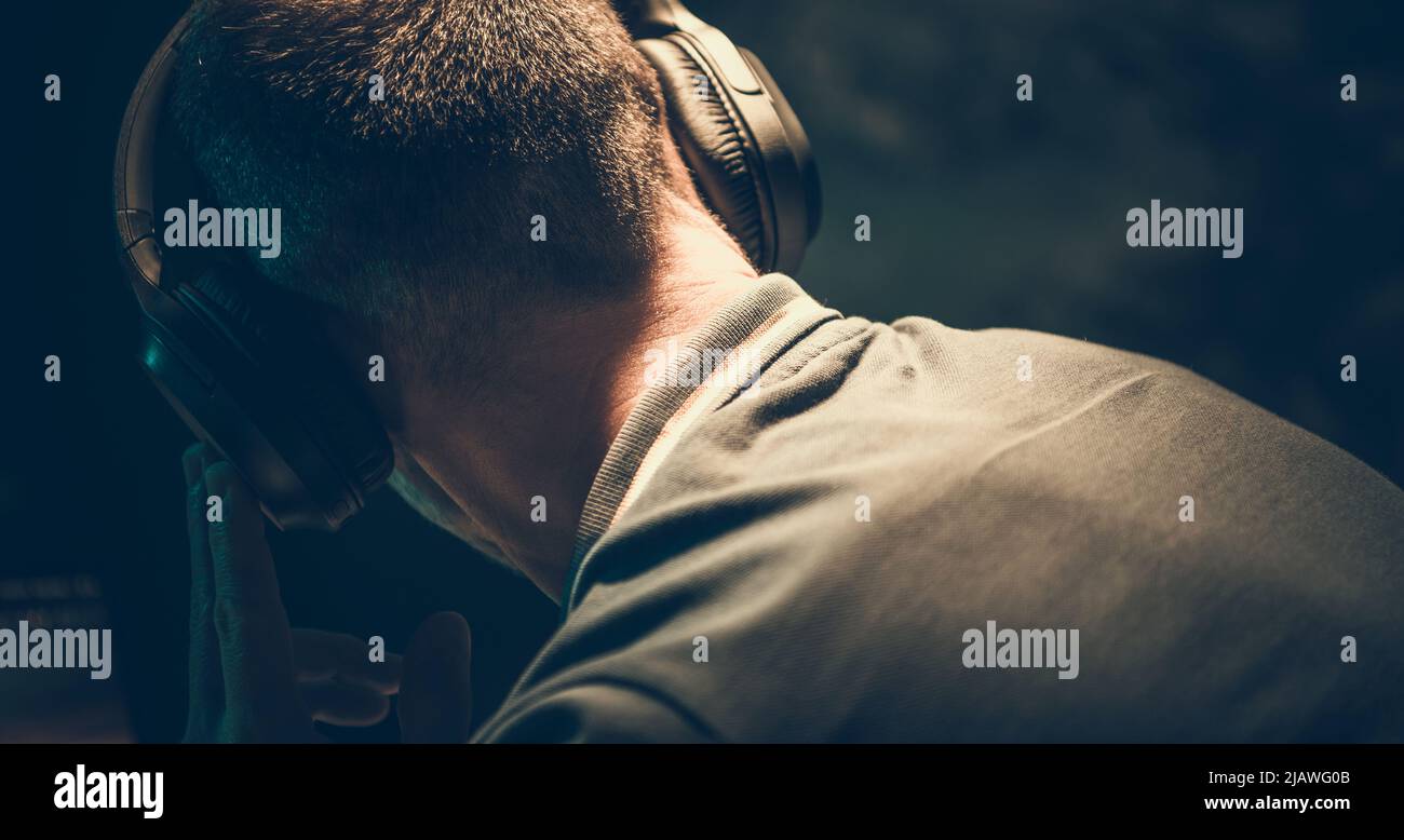 Uomini caucasici che ascoltano musica utilizzando cuffie wireless all'interno di una stanza oscura. Foto Stock