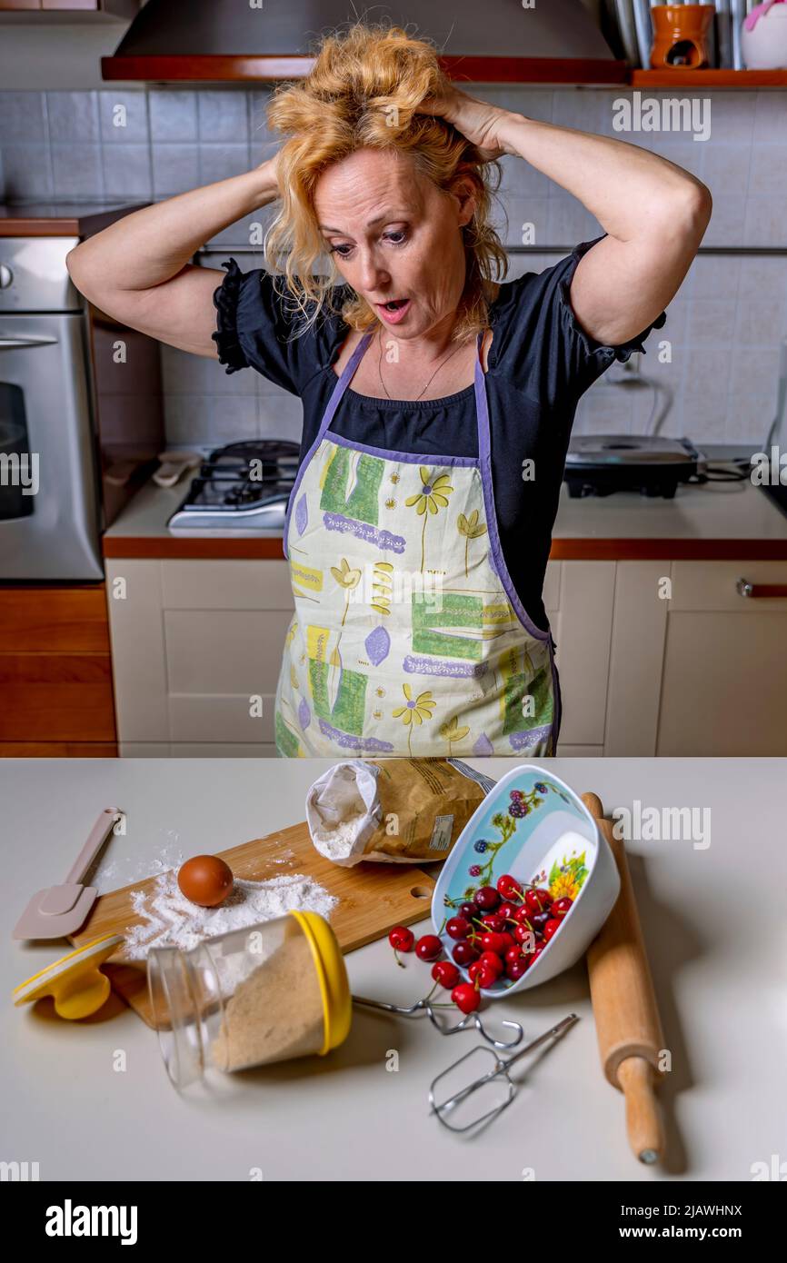 Disperata casalinga con le mani nei capelli per il disordine in cucina, che dovrà ripulire Foto Stock