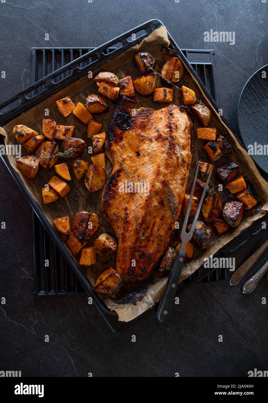 Piatto da forno con filetto di mezza salmone arrostito e caramellato. Cucinato con patate e servito su una teglia da forno su sfondo scuro del tavolo. Vista dall'alto Foto Stock