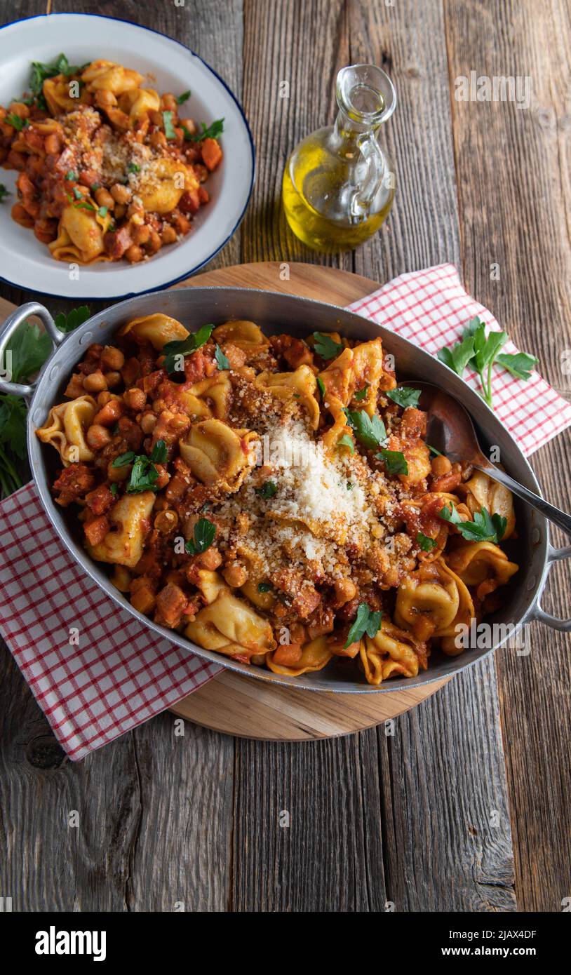 Piatto di pasta italiana con tortellini, pancetta, ceci, verdure e salsa di pomodoro. Condito con parmigiano e servito in una padella rustica Foto Stock