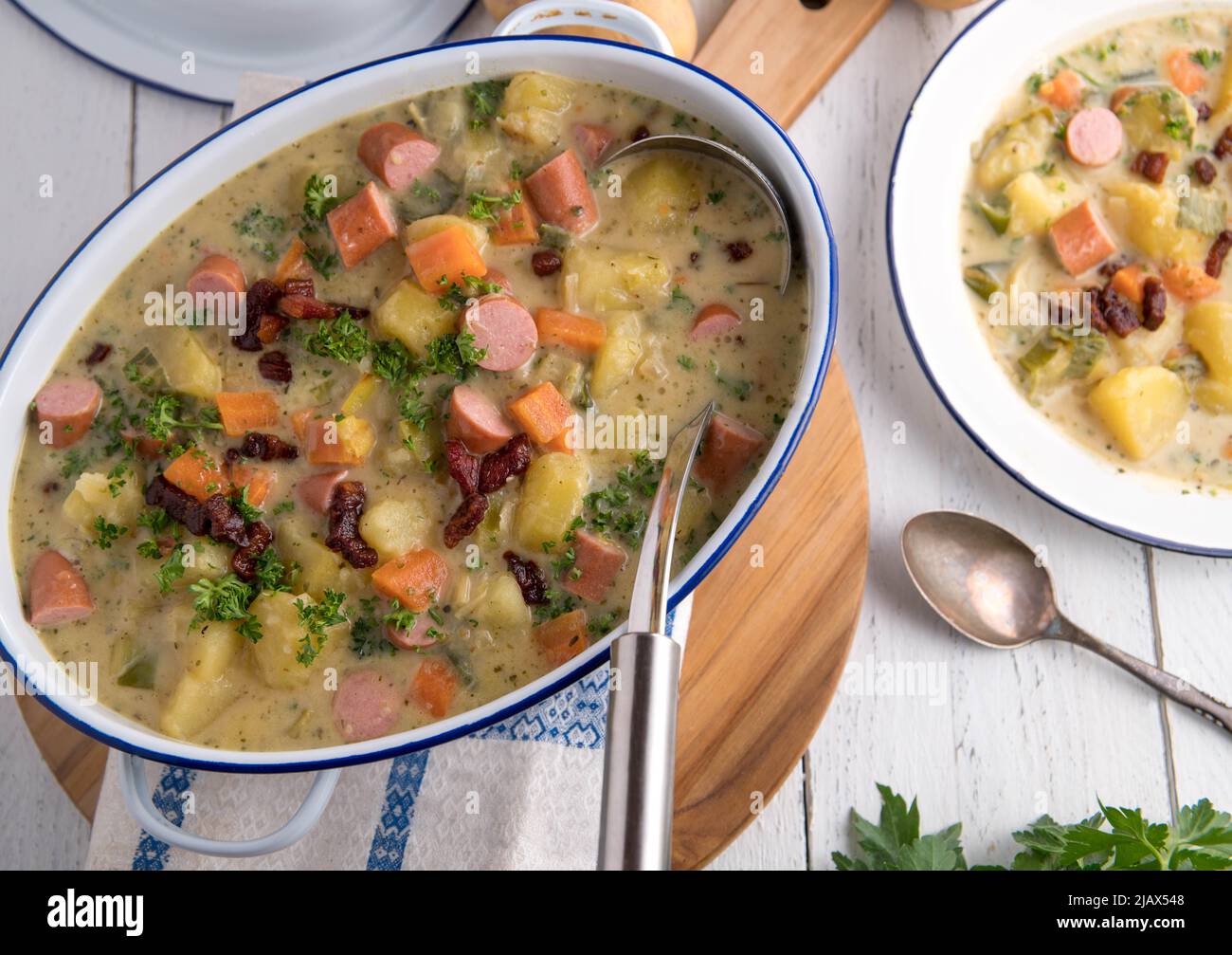 Pentola con zuppa di patate, pancetta croccante e salsiccia bollita. Servito su sfondo vecchio stile e bianco Foto Stock