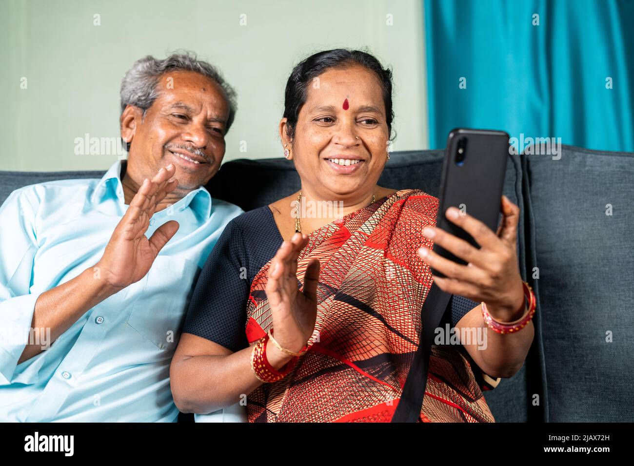 Coppia anziana impegnata a fare videochiamate sul cellulare da casa - concetto di comunicazione, tecnologia e stile di vita attivo. Foto Stock