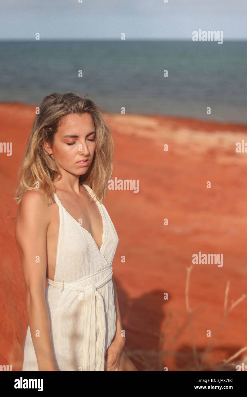 Primo piano ritratto di bella giovane bionda donna in abito bianco su spiaggia di sabbia rossa sulla costa occidentale dell'Australia Foto Stock