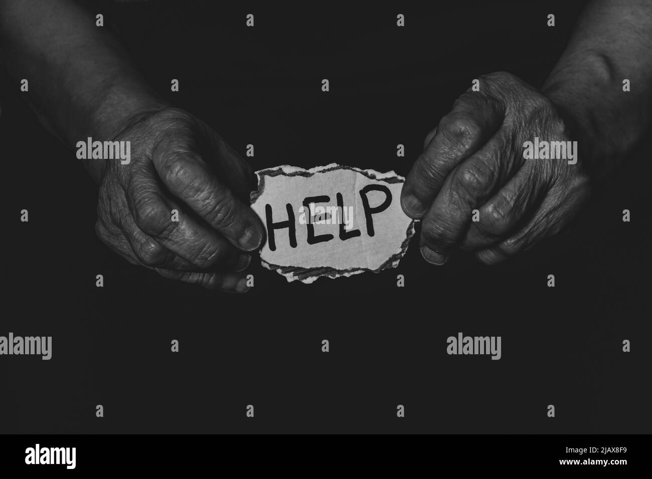 Le vecchie mani femminili tengono un pezzo di carta con testo di aiuto nel buio, aiutano le persone nel bisogno, una persona nel bisogno Foto Stock