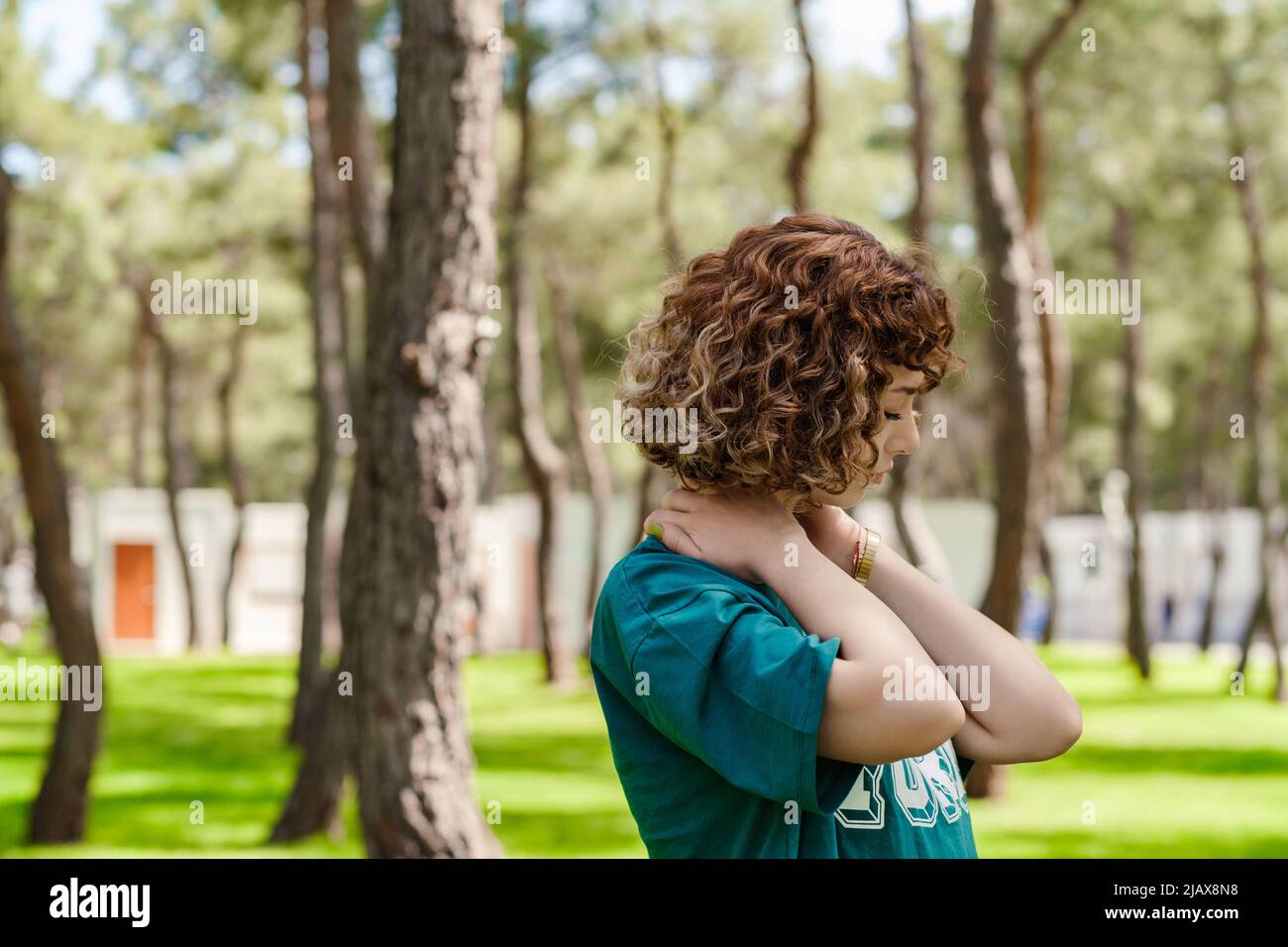 Vista laterale della giovane donna rossa in piedi sul parco cittadino, all'aperto sensazione di dolore alle spalle articolare dolore alla schiena, concetto di fibromialgia, vista posteriore ravvicinata. Foto Stock
