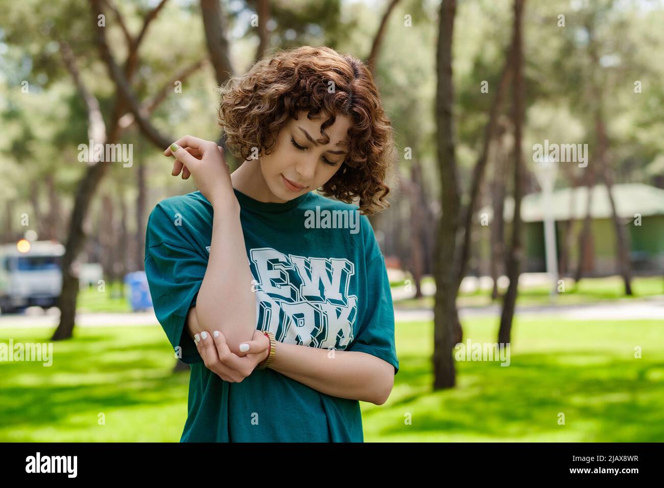 Giovane donna rossa che indossa una maglietta verde che soffre di reumatismi cronici articolari. Dolore al gomito e concetto di trattamento. Sanità e medicina. Foto Stock