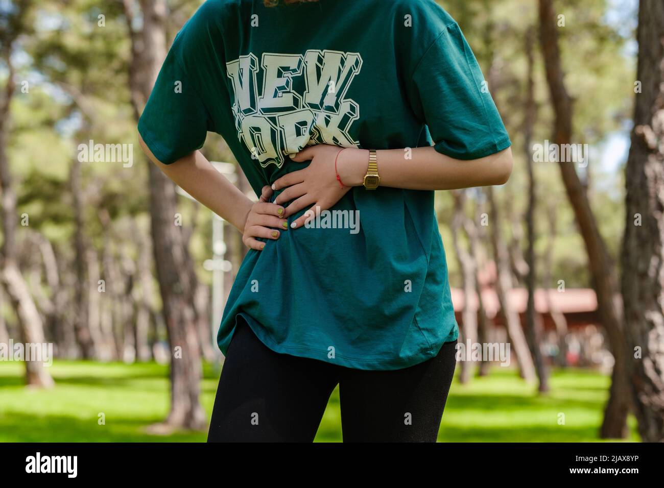 Vista ritagliata di giovane donna sportiva che indossa una t-shirt verde e un leggio nero in piedi sul parco cittadino, all'aperto con mano sullo stomaco perché indigestione, Foto Stock