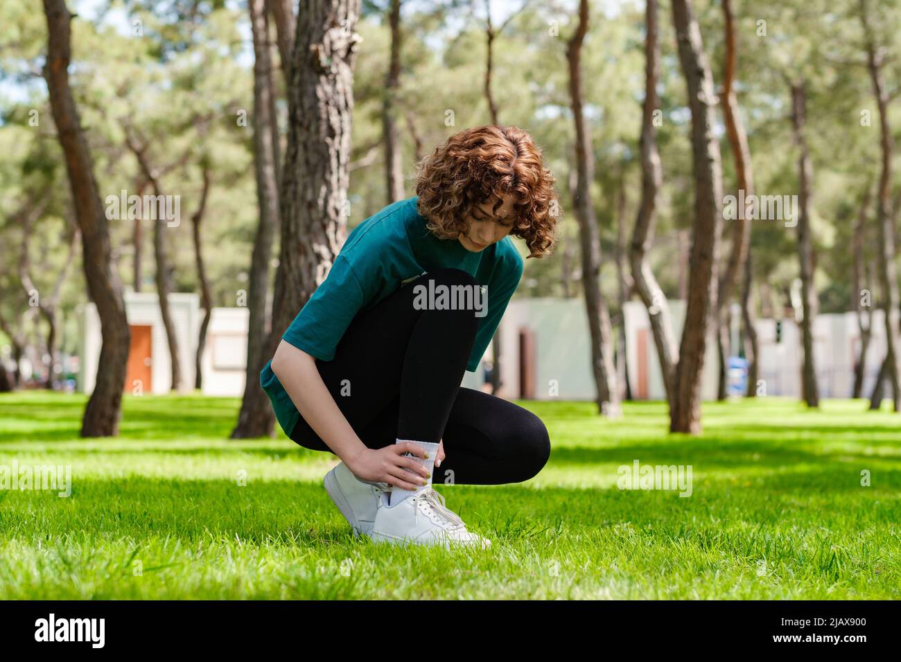 Giovane donna rossa che indossa una t-shirt verde e leggings neri che soffrono di una lesione alla caviglia durante l'esercizio e la corsa. Concetto di salute e sport Foto Stock