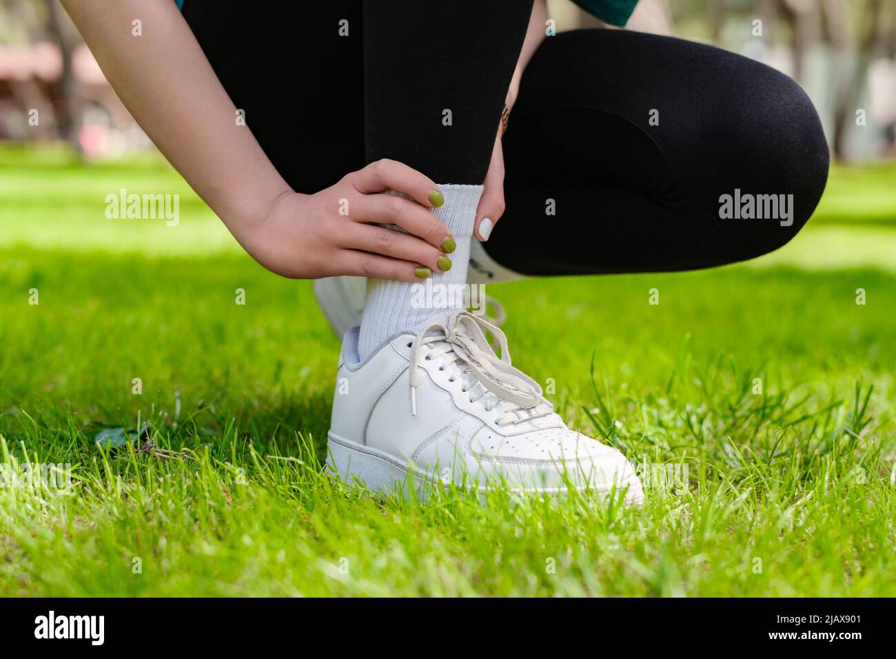 Vista ravvicinata della giovane donna che indossa leggings neri affetti da una lesione alla caviglia durante l'esercizio e la corsa. Concetto di salute e sport. Foto Stock