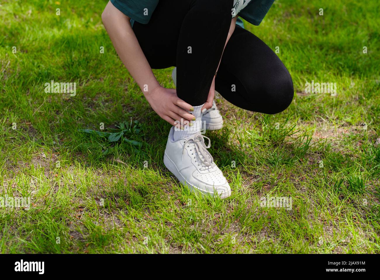 Vista ritagliata di giovane donna runner indossando leggings neri che soffrono di una lesione alla caviglia durante l'esercizio e la corsa. Concetto di salute e sport. Foto Stock
