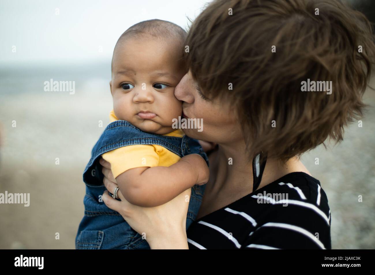 Neonato bambino multirazziale tenuto e baciato dalla madre Foto Stock