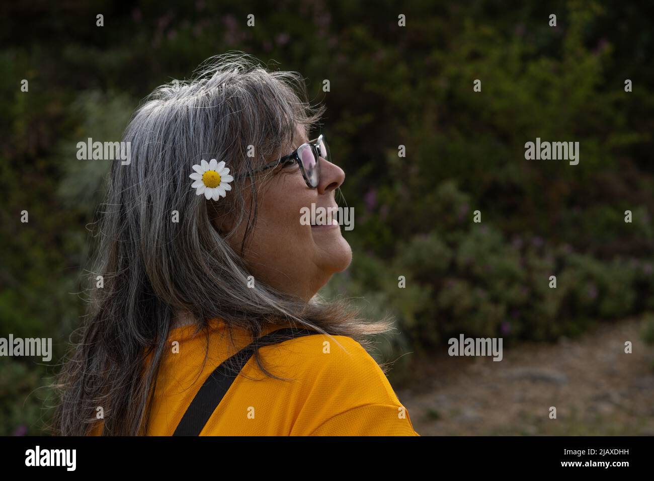 donna dai capelli bianchi che indossa occhiali con una margherita nei capelli Foto Stock