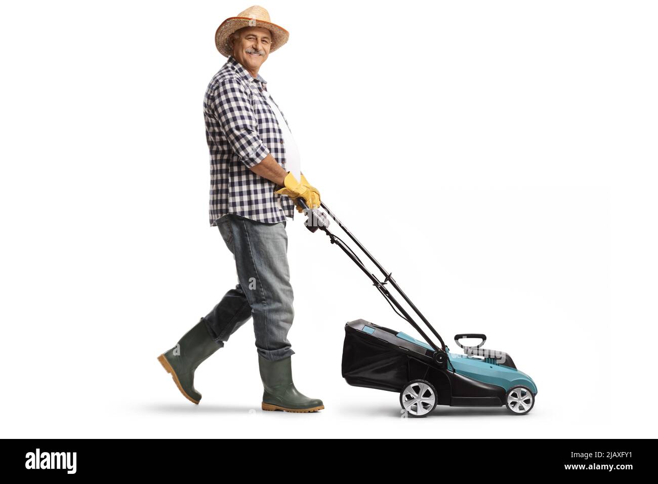 Colpo di profilo a tutta lunghezza di un uomo maturo con un cappello di paglia e stivali utilizzando un rasaerba isolato su sfondo bianco Foto Stock