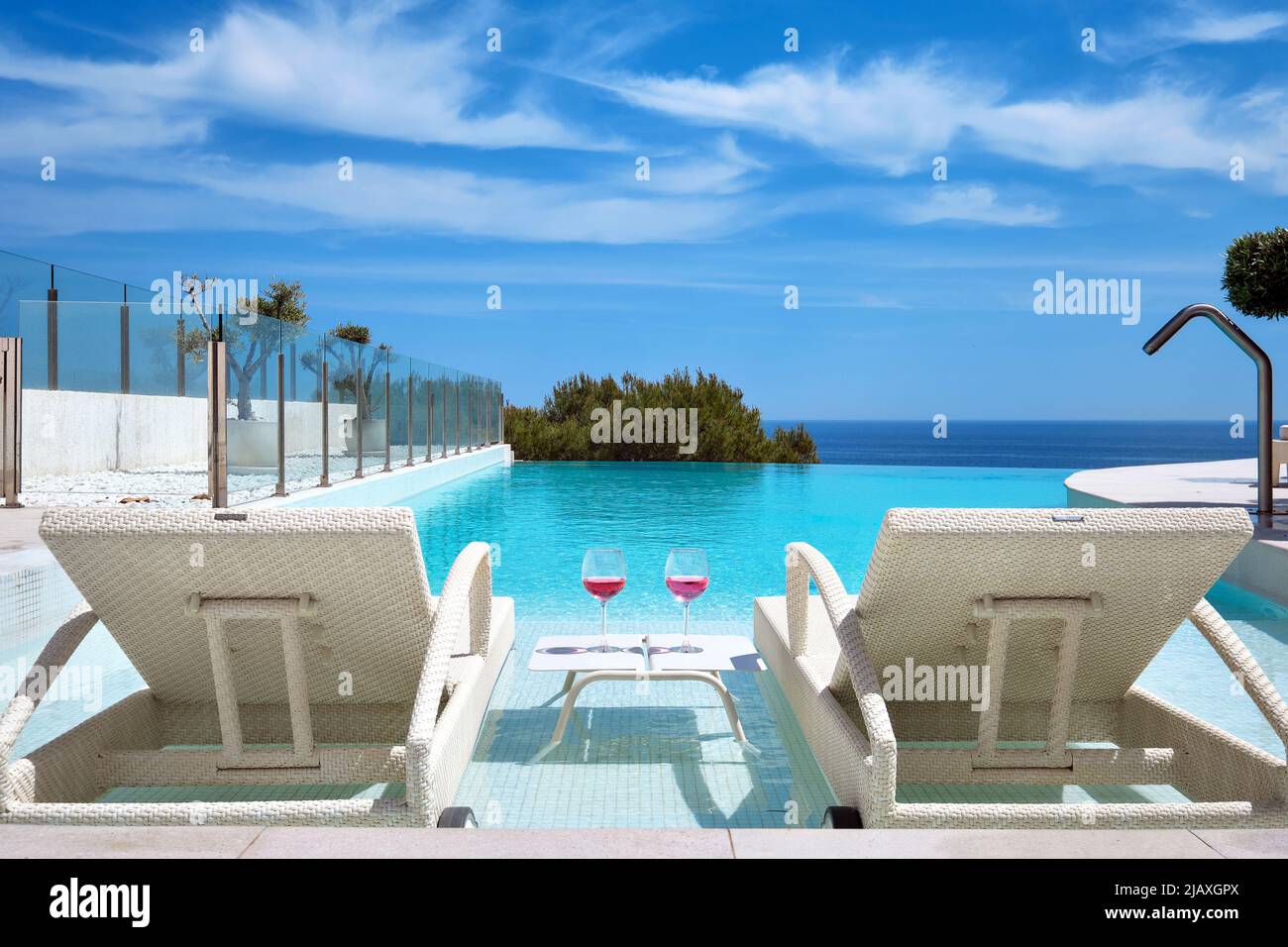 Due bicchieri con cocktail sul tavolo tra sedie a sdraio lettini in piscina, mare, cielo blu sfondo a bordo piscina. Vacanze estive, concetto di relax Foto Stock
